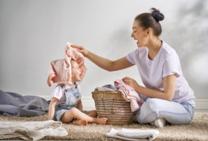 Beautiful young woman and child girl little helper are having fun and smiling while doing laundry at home.